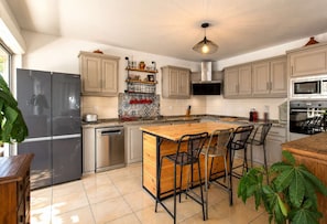 A modern kitchen with a central island, bar stools, a dishwasher, a refrigerator, a microwave, and a stove. - VILLA MAÏDIANA - villa 10 pers. piscine chauffée à 200 m du lagon de La Saline-les-Bains (Saint-Gilles-Les-Bains)