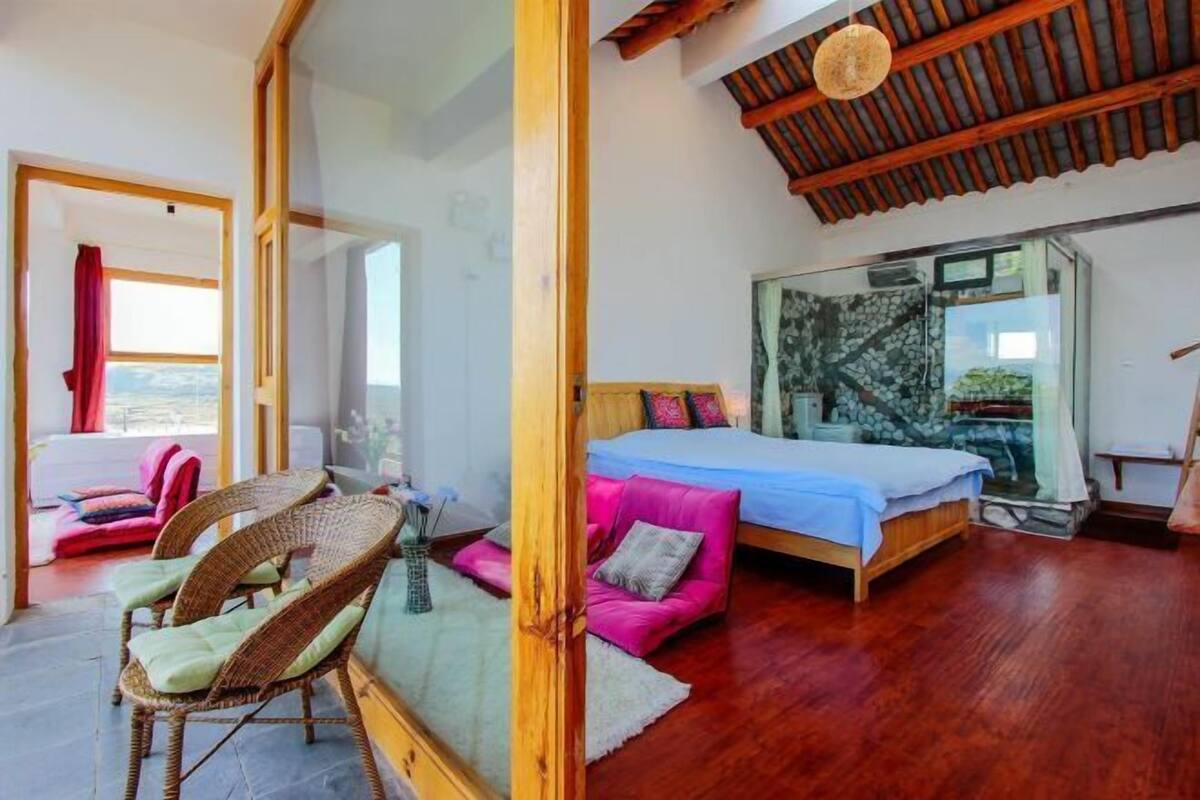 A bedroom with a bed, a sofa, and a chair. There is a window with a view of the outside.