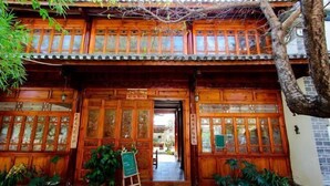 A traditional wooden building with large wooden doors and windows, a small entrance, and potted plants in front. - Gospel Hostel (Dali City)