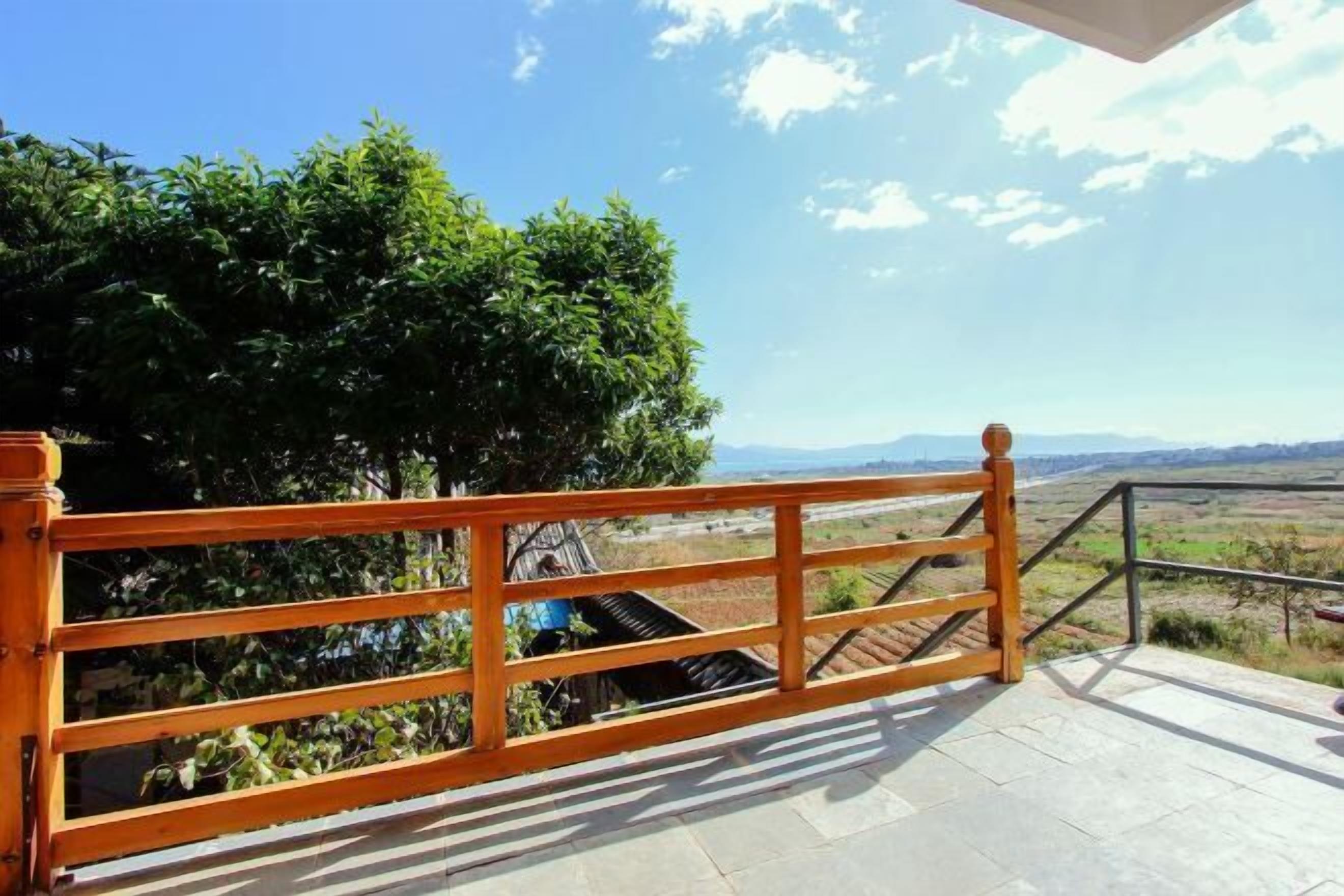 Un balcón de madera con vistas a un paisaje, que incluye árboles y montañas distantes.