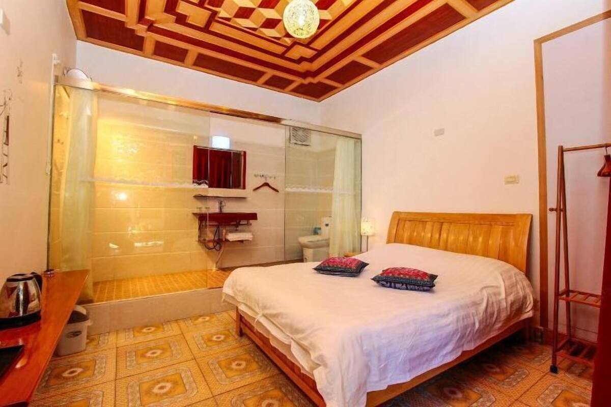 A bedroom with a wooden headboard, a bed with white bedding, a glass shower enclosure, and a patterned floor.