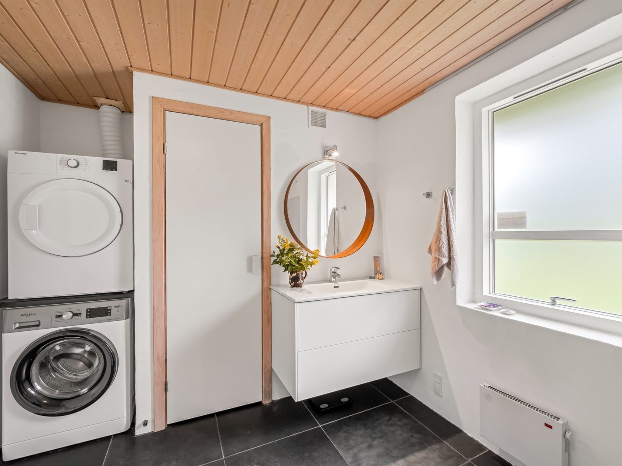 Une petite salle de bain équipée d’un lave-linge, d’un miroir et d’un radiateur.