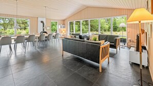 Ett rymligt vardagsrum med modern design, inrett med en stor soffa, ett matbord och stolar, och stora fönster som ger utsikt över omgivningen.