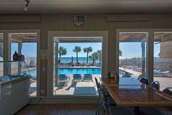 A room with a view of a pool and beach chairs, a table, and a sign reading "Beach House".