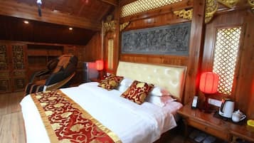 A traditional wooden room with a bed, pillows, a chair, and a table with a lamp.