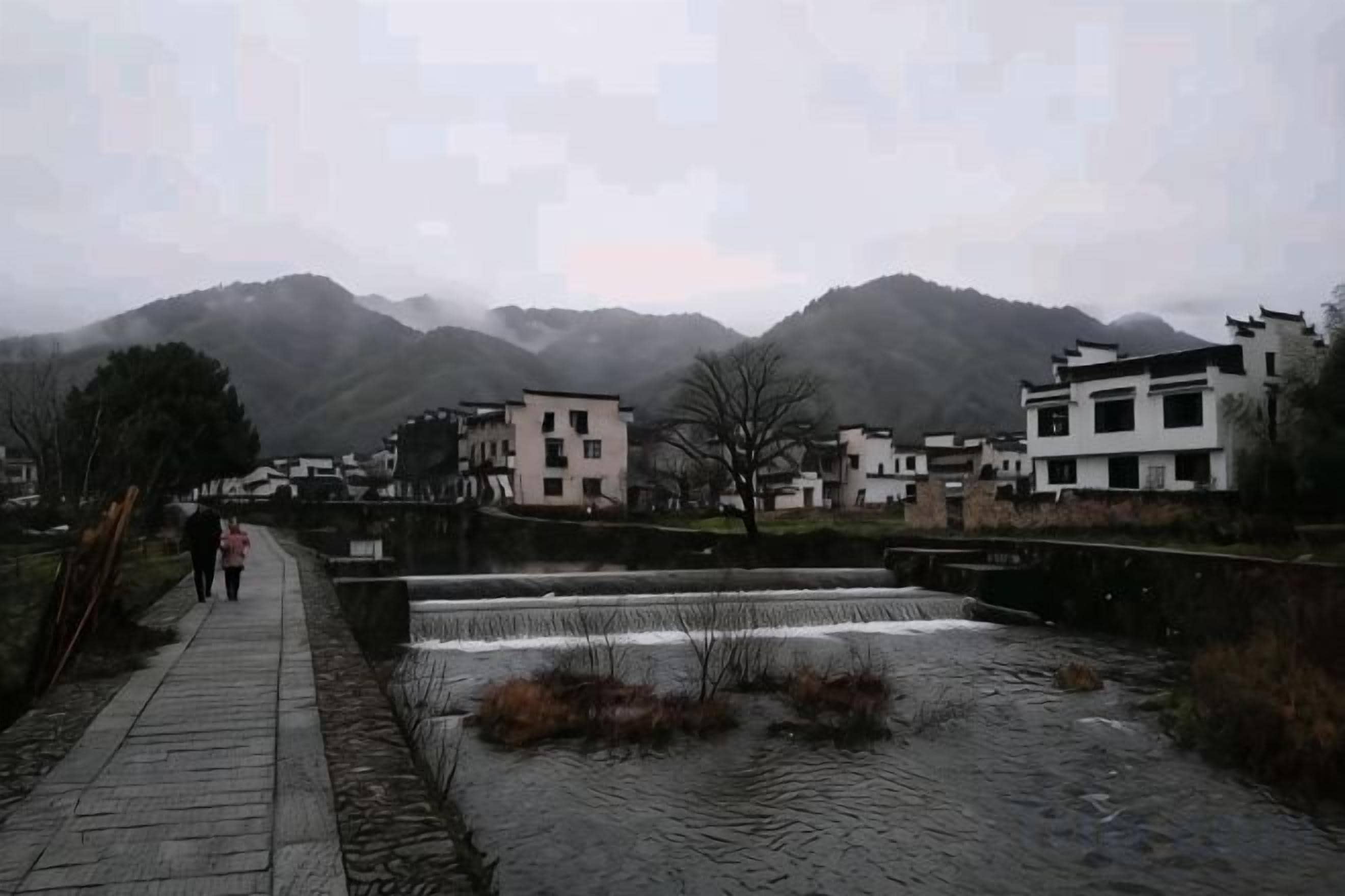 A paved walkway beside a water feature with buildings in the background.