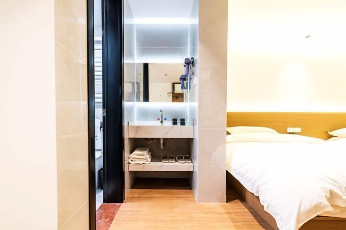 Une chambre d’hôtel avec un lit, une salle de bain avec un miroir et une étagère contenant des articles de toilette.