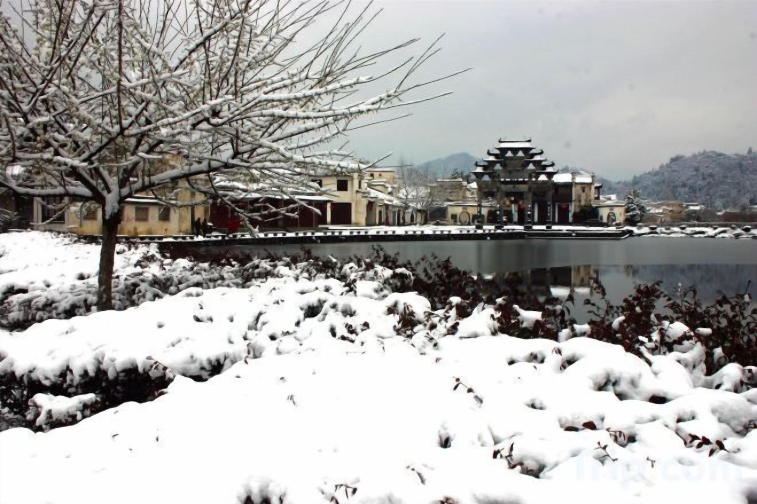 A traditional building with a reflection in a body of water, surrounded by snow-covered ground.