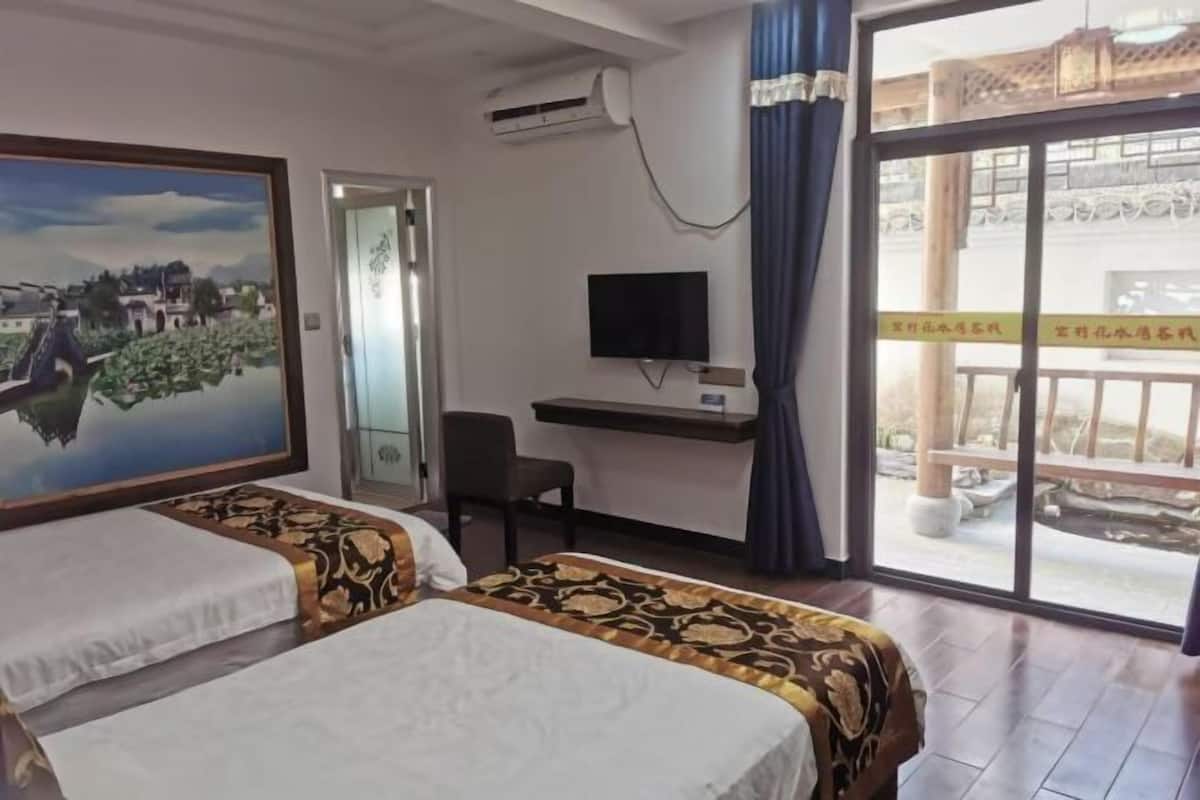 Une chambre d’hôtel avec deux lits, un bureau avec un ordinateur, une télévision et une grande fenêtre donnant sur un bâtiment traditionnel et un pont.