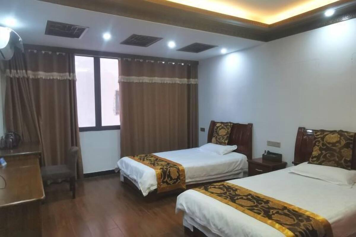 Une chambre d’hôtel avec deux lits, un bureau, une chaise et une fenêtre avec des rideaux.