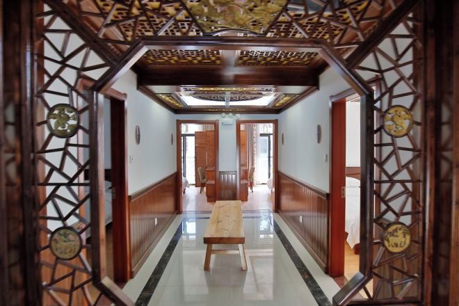 A corridor with a wooden bench, a patterned ceiling, and a view into another room.