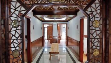 A corridor with a wooden bench, a patterned ceiling, and a view into another room.