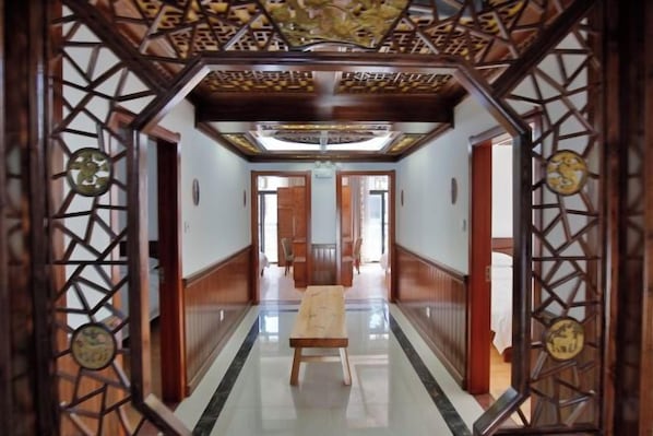 Un couloir avec un banc en bois, un plafond orné de motifs et une vue sur une autre pièce.