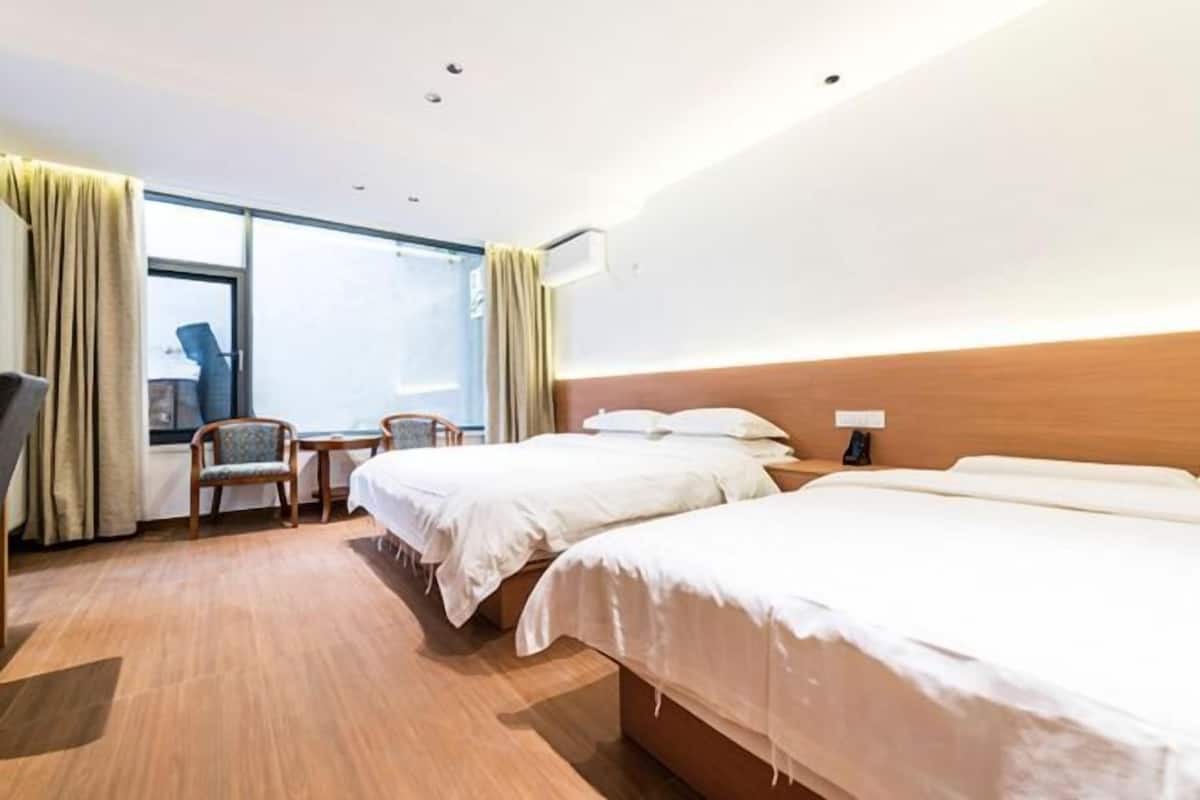 Une chambre d’hôtel avec deux lits, un bureau, une chaise et une fenêtre avec des rideaux.