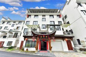 Un immeuble à plusieurs étages de style architectural chinois traditionnel, avec une entrée rouge ornée de caractères chinois, des balcons et un ciel dégagé.