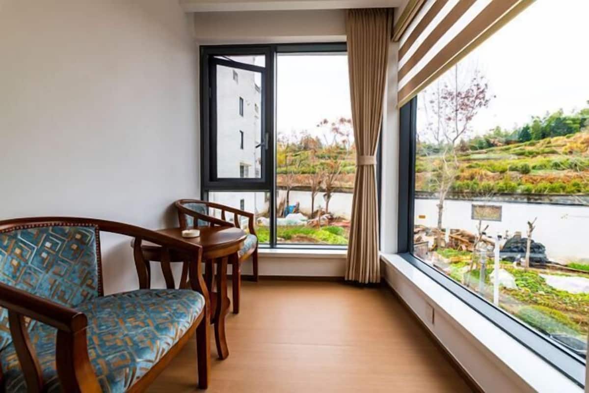 Une pièce comprenant un canapé, une petite table et une fenêtre donnant sur un lac et la verdure environnante.