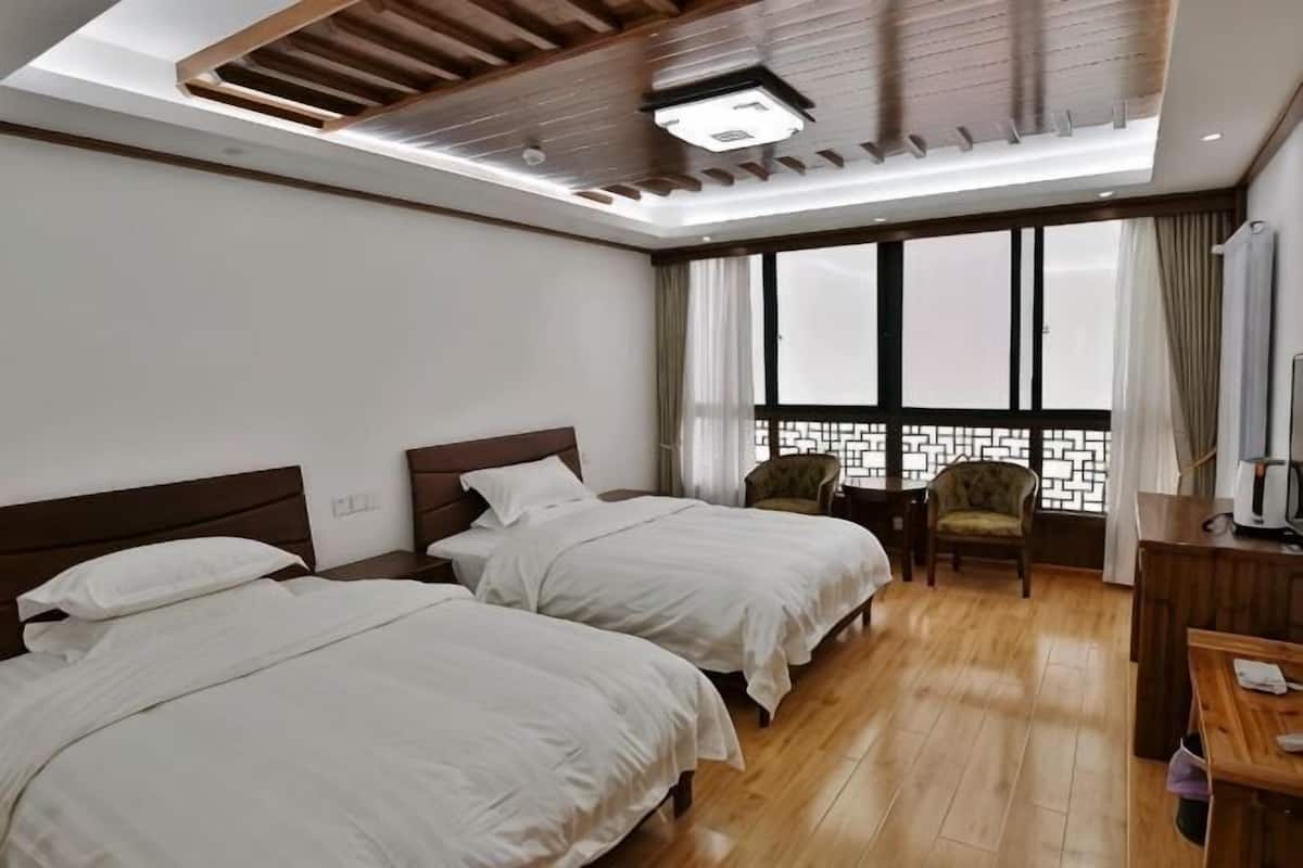 Une chambre d’hôtel avec deux lits, un bureau, une chaise et une grande fenêtre donnant sur un beau paysage.