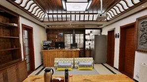 A room with a wooden table, a coffee maker, and a kettle. There is a kitchen area with a refrigerator and a microwave in the background. - Yi Xuan Ju Deluxe Lnn and Suites (Yi County)