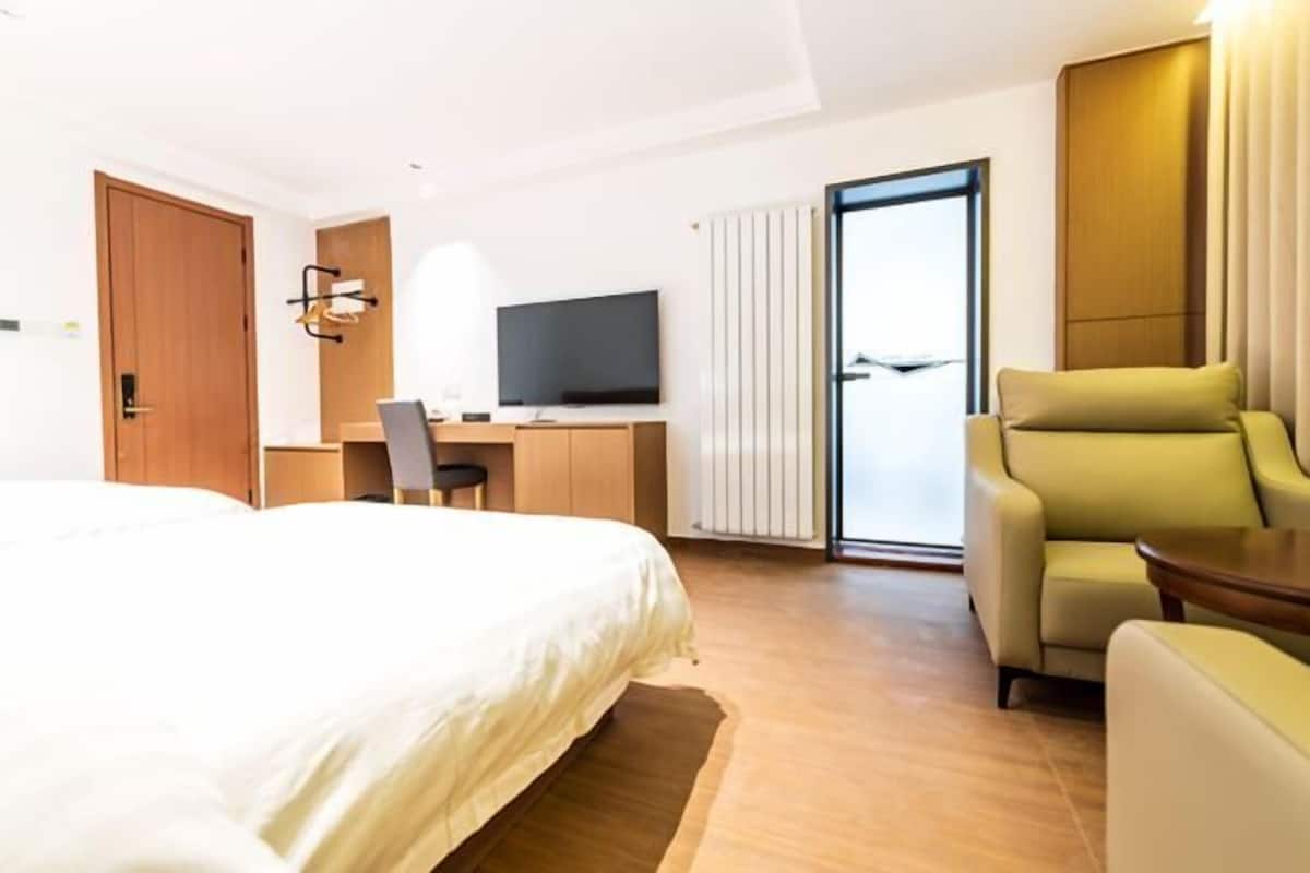 Une chambre d’hôtel avec un lit, un bureau avec une télévision, une chaise et une vue à travers une porte vitrée.