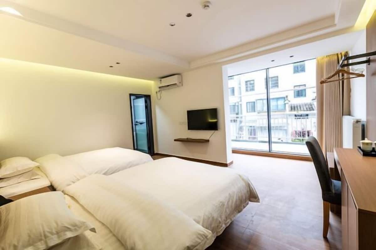 Une chambre d’hôtel avec deux lits, une télévision, un bureau et une grande fenêtre donnant sur des immeubles.