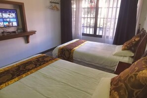 Een hotelkamer met twee bedden, een televisie op een plank en een raam met gordijnen.