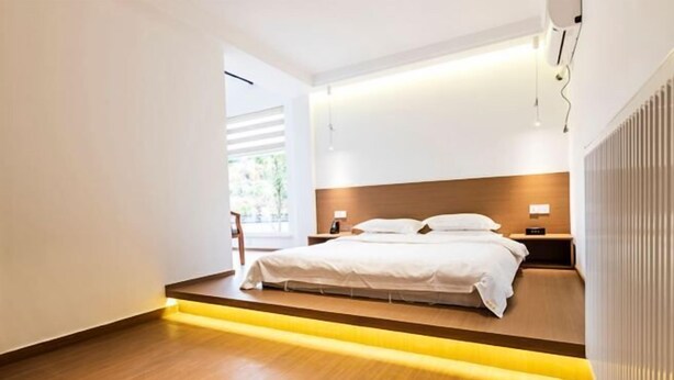 A modern hotel room with a wooden floor, a bed with white linens, a nightstand, and a bedside table with a lamp. - Yi Xuan Ju Deluxe Lnn and Suites (Yi County)