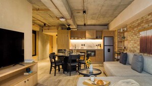A modern living room with a flat-screen TV, a dining area with a round table and chairs, a kitchen with wooden cabinets, and a grey sofa. - Caliza Roma | Exclusive Residence w/Private Garden (Ciudad de México)