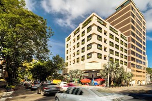 A multi-story hotel with balconies, a street view, and palm trees.