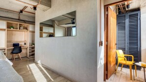 Una habitación con cama, escritorio, silla, espejo y una puerta que da a otra estancia.