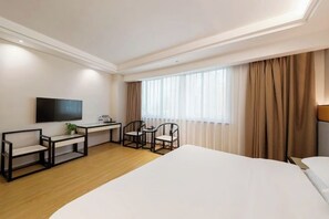 Habitación de hotel con una cama grande, un escritorio con sillas, un televisor de pantalla plana y una ventana con cortinas.