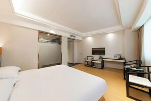Une chambre d’hôtel avec un grand lit, un bureau avec une chaise, une télévision et une porte donnant sur une salle de bain.
