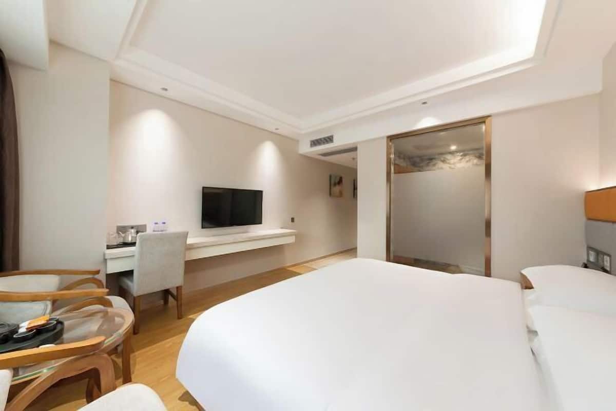 A hotel room with a bed, a desk with a flat-screen TV, a chair, and a glass table.