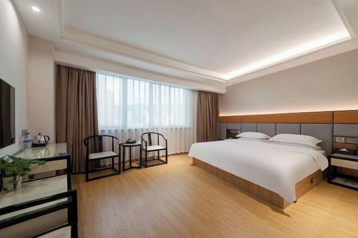 A hotel room with a bed, a desk, a chair, a TV, and a window with curtains.