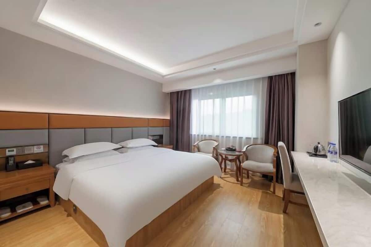 A hotel room with a bed, bedside table, desk, chairs, and a TV.