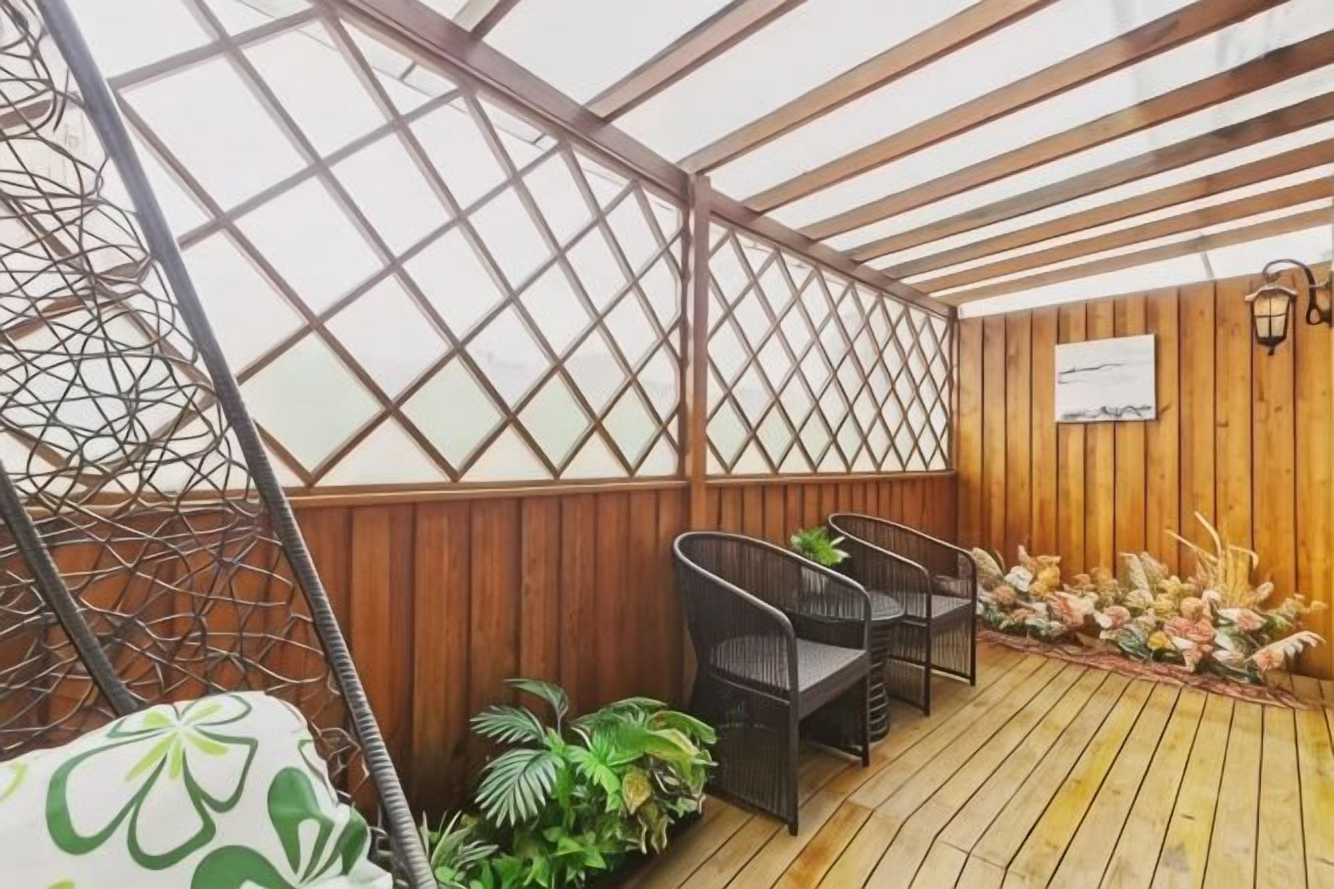 A covered outdoor seating area with a wooden floor, a swing chair, and two wicker chairs.