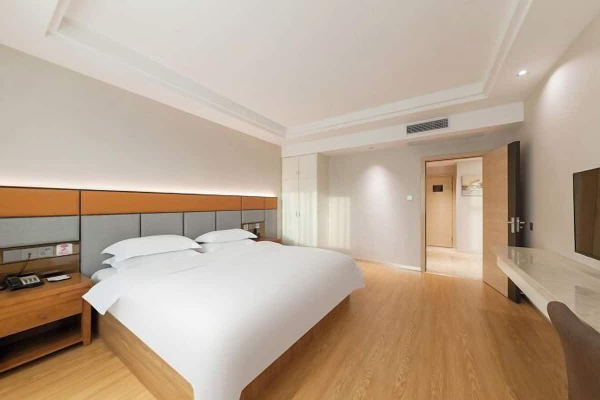 A modern hotel room with a large bed, wooden flooring, a bedside table with a phone, and a TV on the wall.
