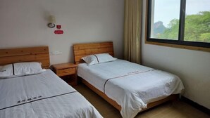 Une chambre d’hôtel avec deux lits simples, une tête de lit en bois, une table de chevet, une fenêtre avec des rideaux et une horloge murale.