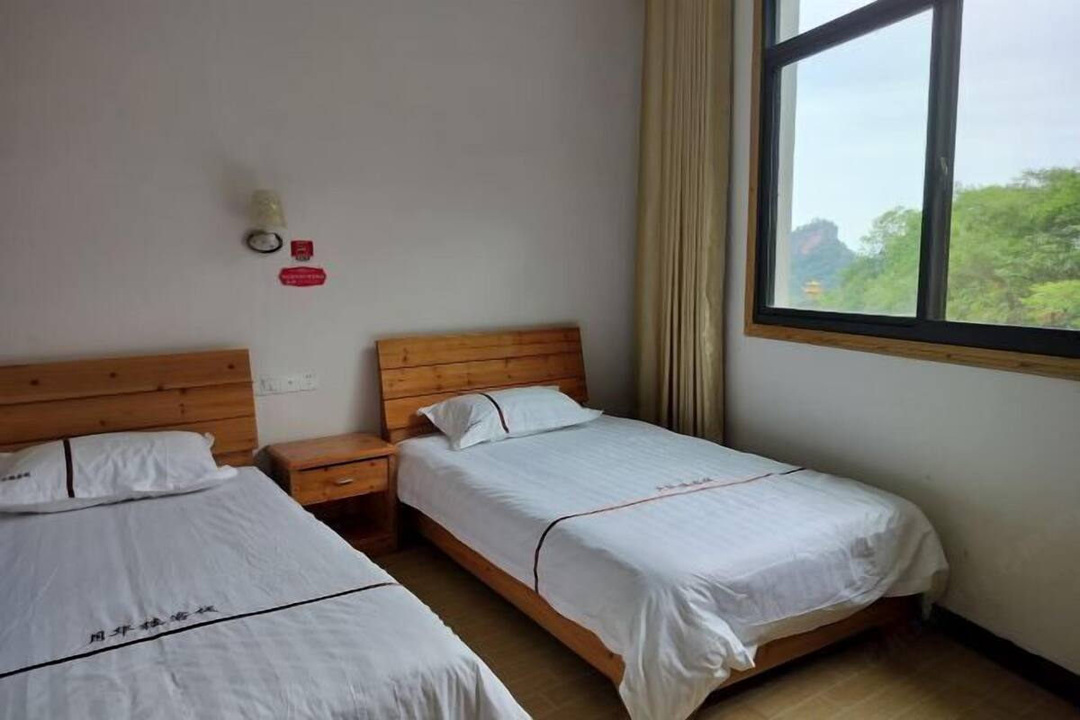 Quarto de hotel com duas camas de solteiro, cabeceira de madeira, mesa de cabeceira, janela com cortinas e um relógio de parede.