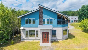 Une maison moderne à deux étages, avec une façade bleue, de grandes fenêtres et un mur d’accent en pierre.