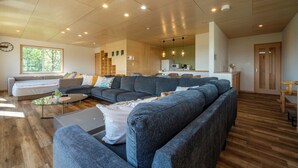 Un salon spacieux avec un grand canapé d’angle, une table basse et un coin cuisine à l’arrière-plan.