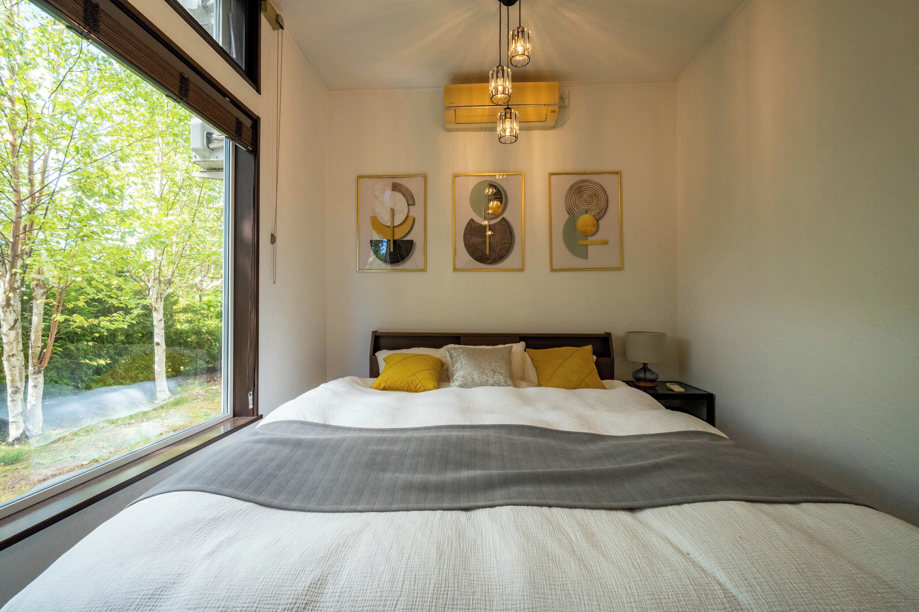 Un dormitorio con una cama grande, una ventana con vistas a árboles y tres obras de arte colgadas en la pared.