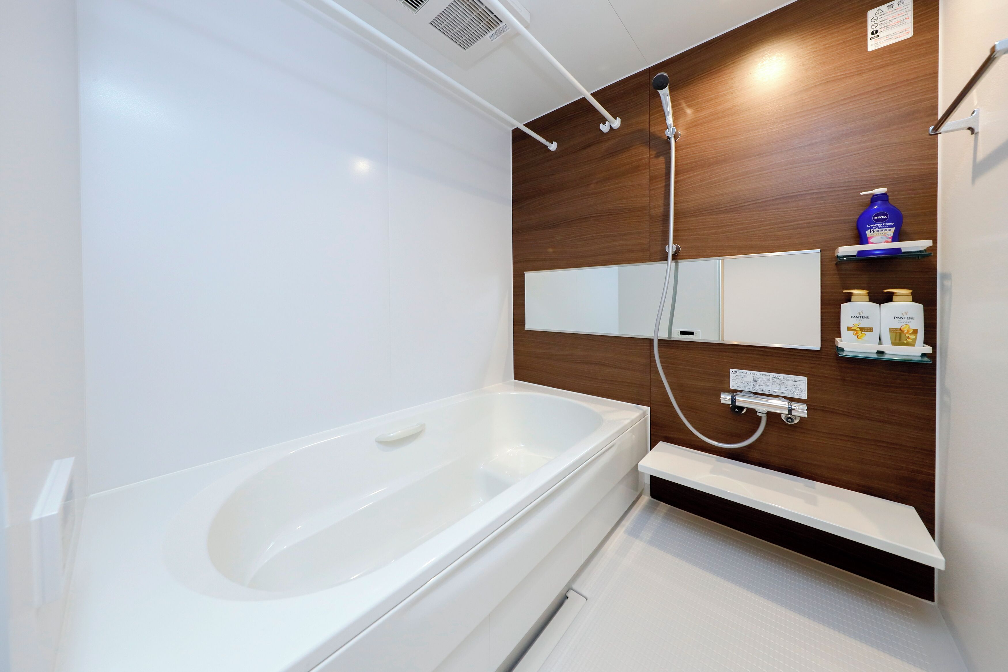 A modern bathroom with a white bathtub, wooden panel wall, and a built-in shelf with toiletries.