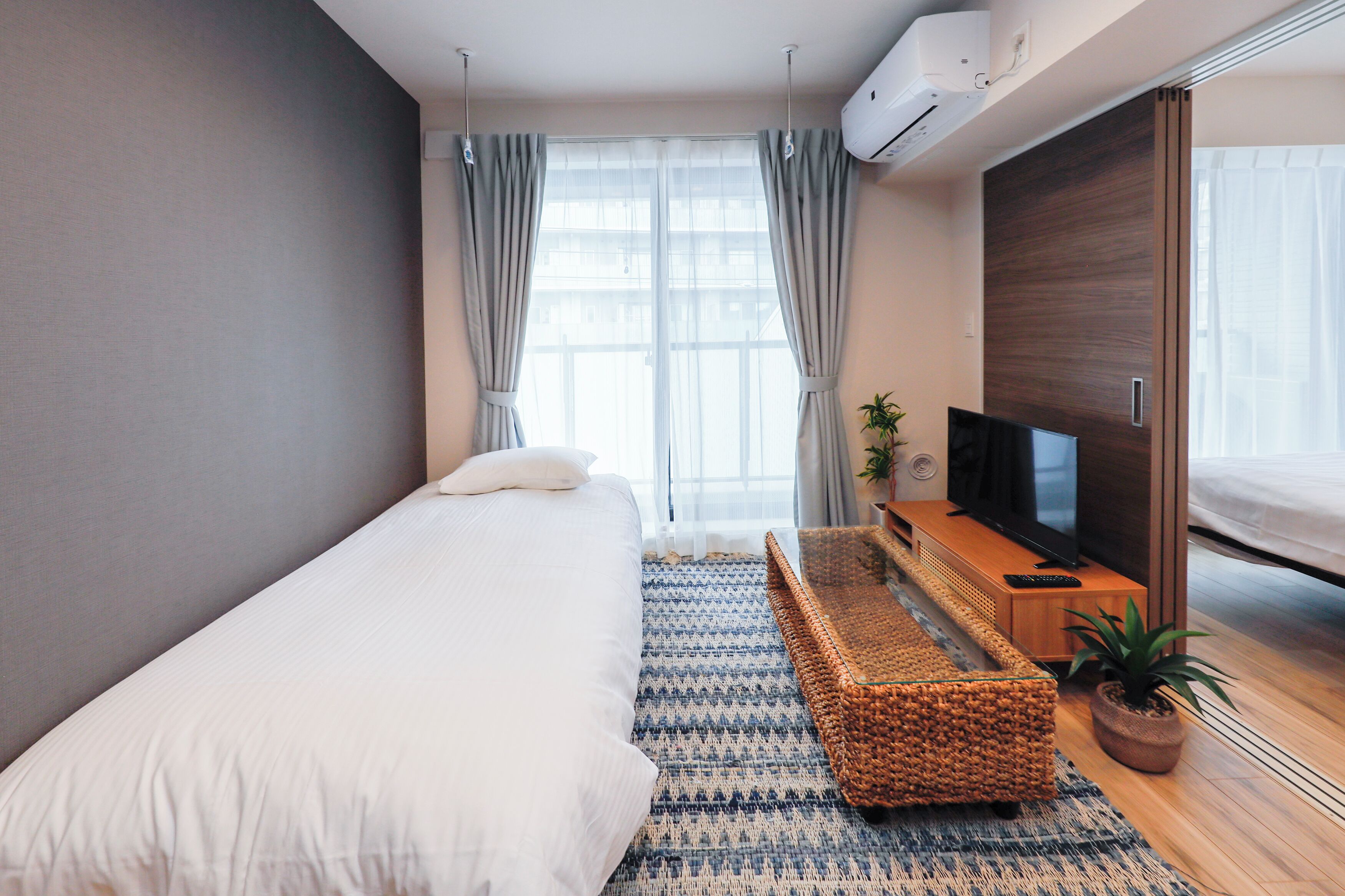 A modern bedroom with a bed, a TV, a wooden cabinet, and a large window with curtains.