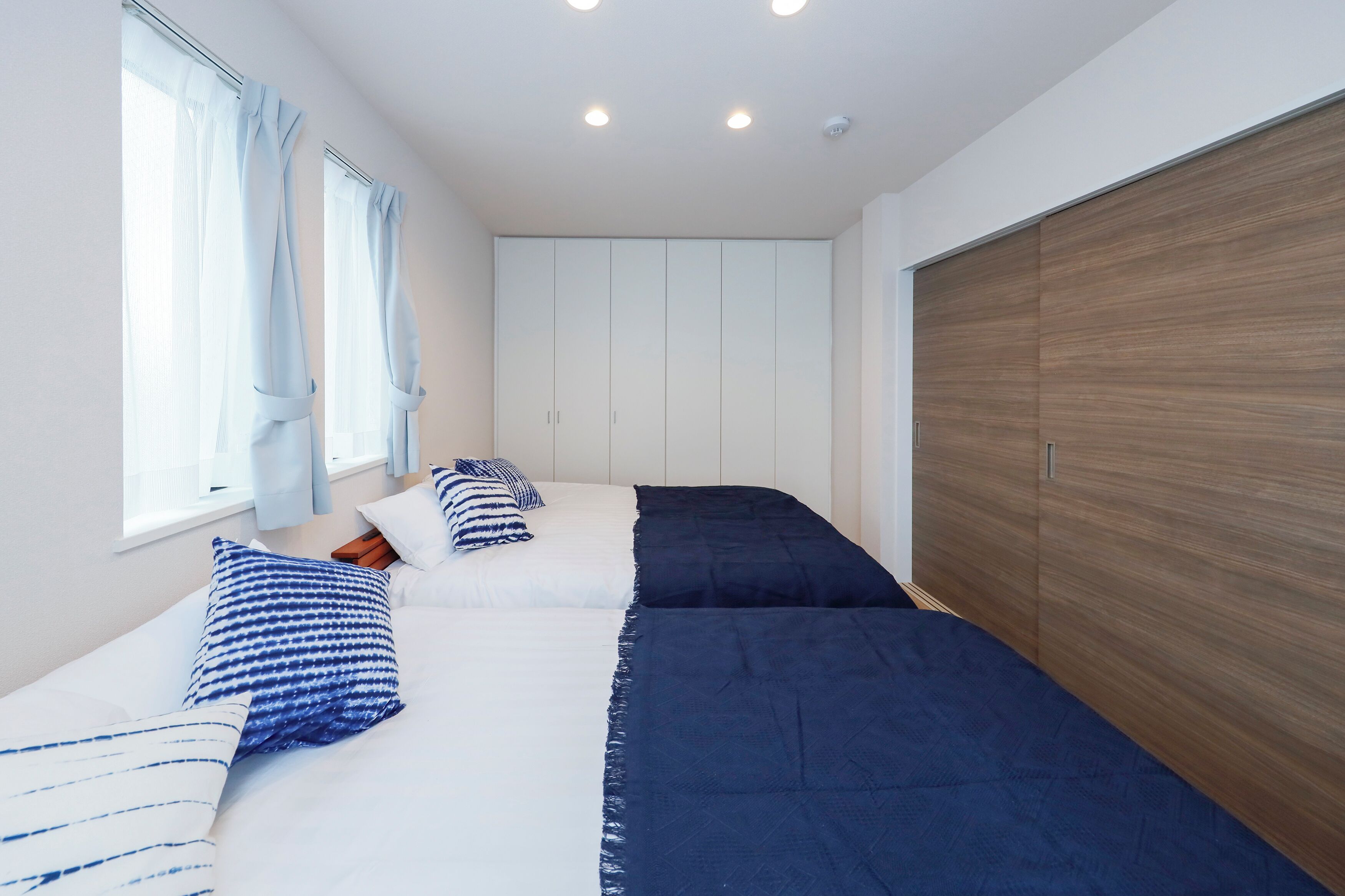 A bedroom with two beds, a wooden wardrobe, and a window with curtains.