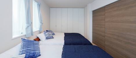 A bedroom with two beds, a wooden wardrobe, and a window with curtains.