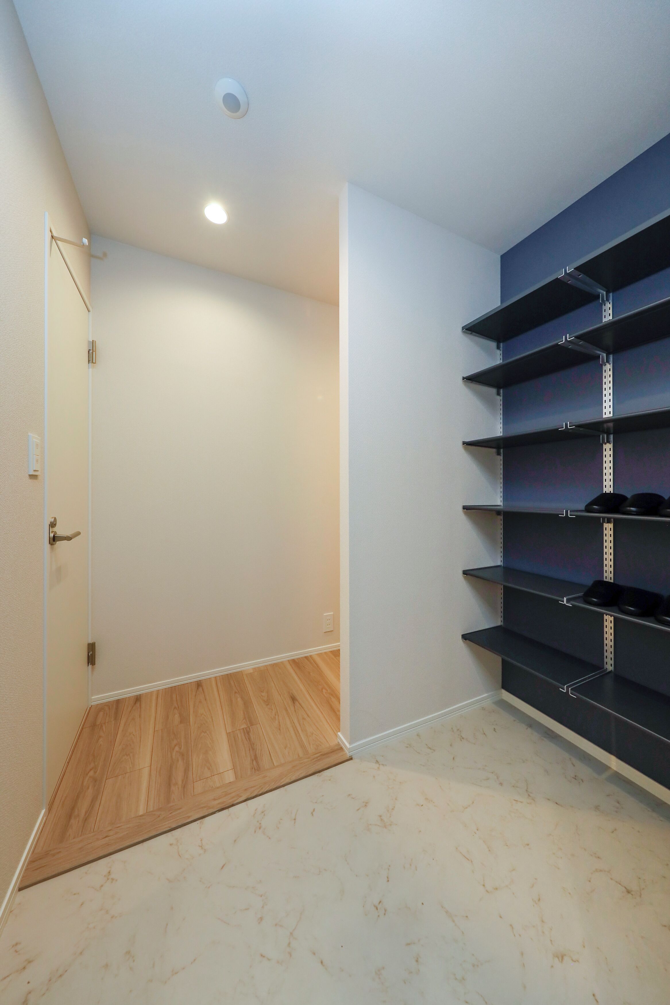 A room with a wooden floor, a white wall, a door, and a shelving unit with shoes.