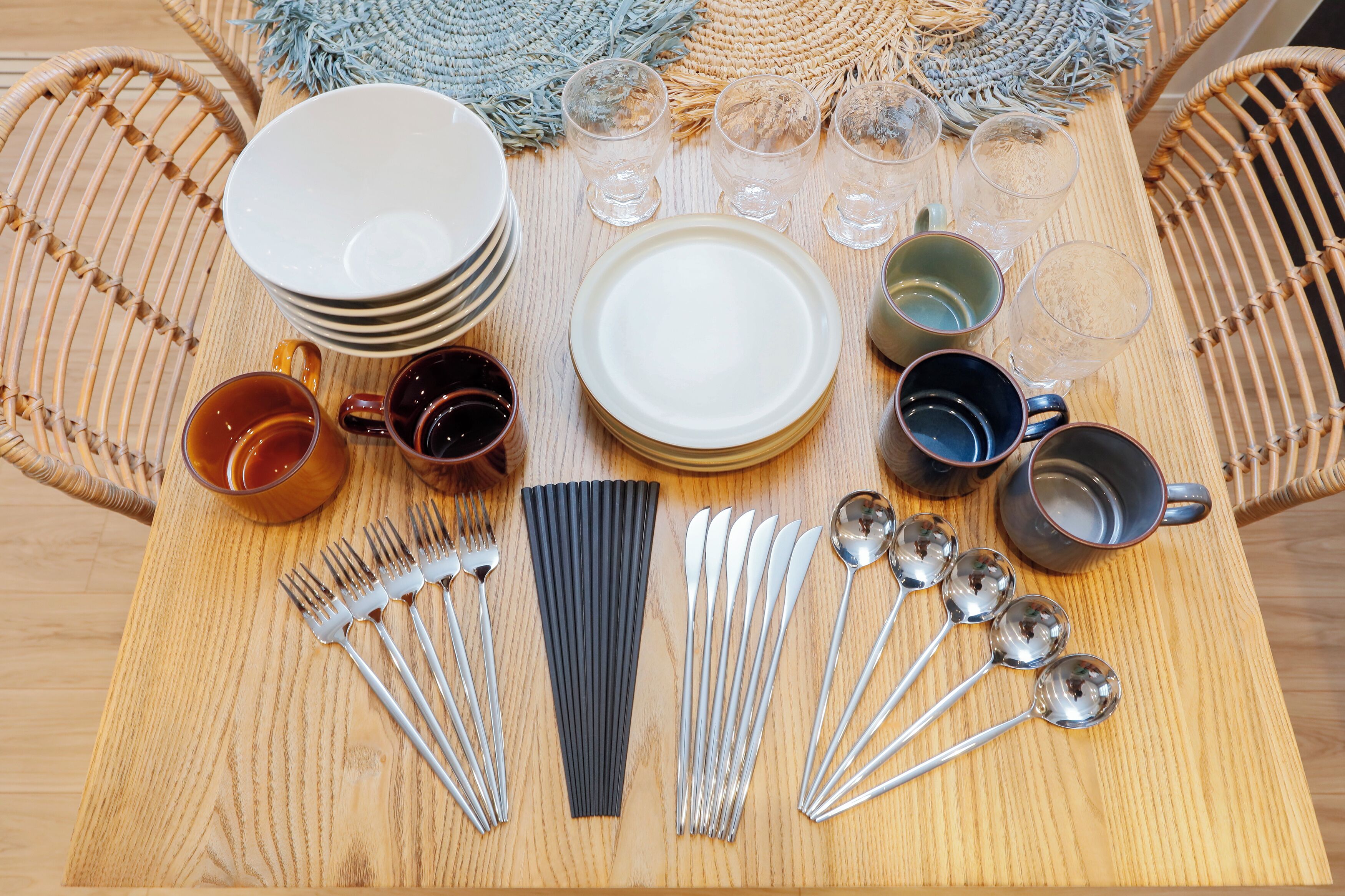 Une table à manger dressée avec des assiettes, des verres, des couverts et un set de table en fibres tressées.
