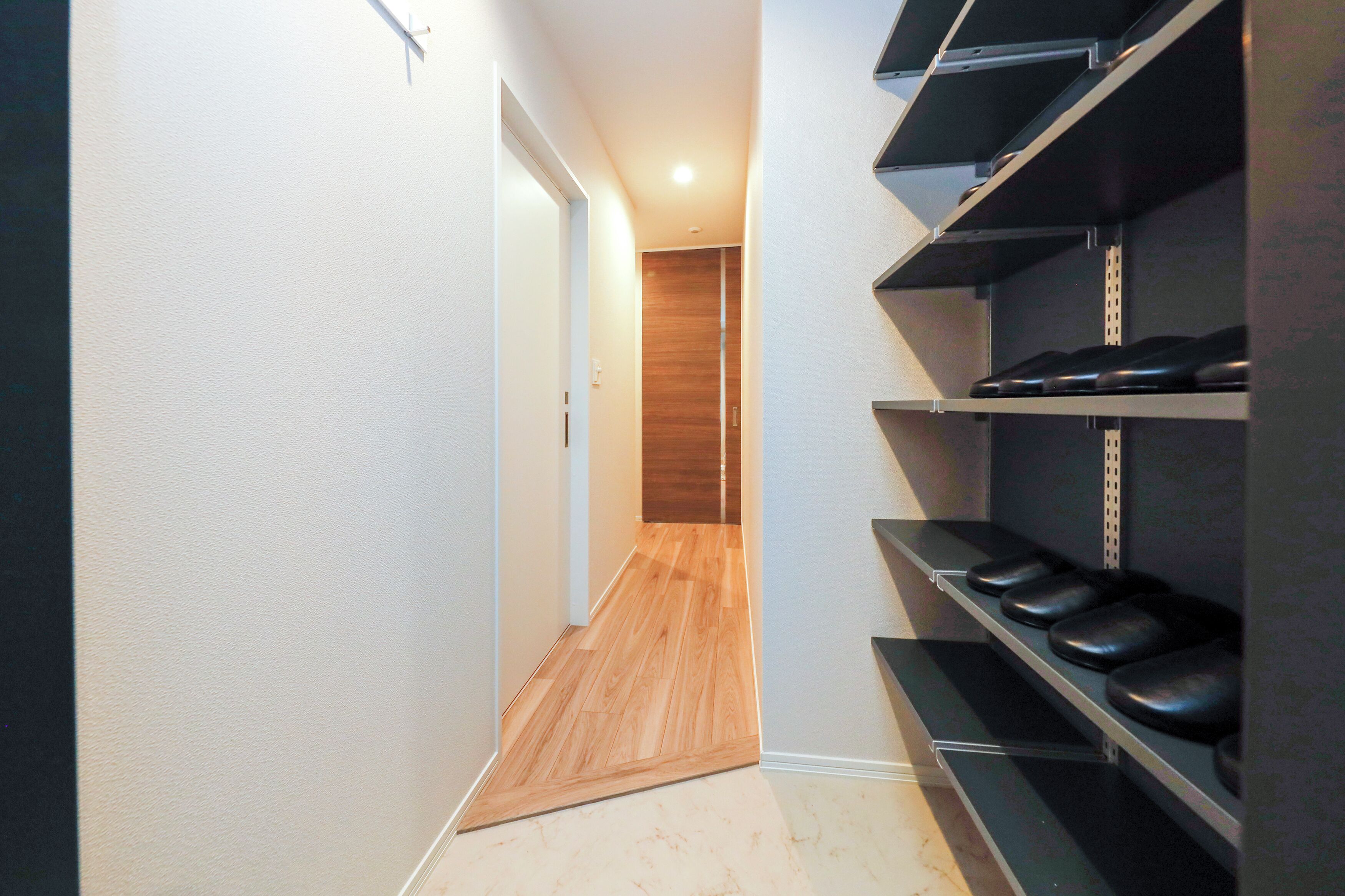 A narrow hallway with wooden flooring, a door at the end, and black shelves on the right.