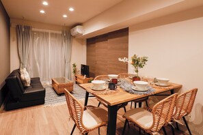 A dining area with a wooden table set for four, surrounded by wicker chairs, a black sofa, and a small side table.