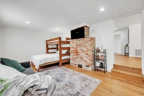 A bedroom with a bunk bed, a brick fireplace, a television mounted above it, a small table with books, and a staircase leading to another room. - Main Street Retreat in Roseville (Roseville)